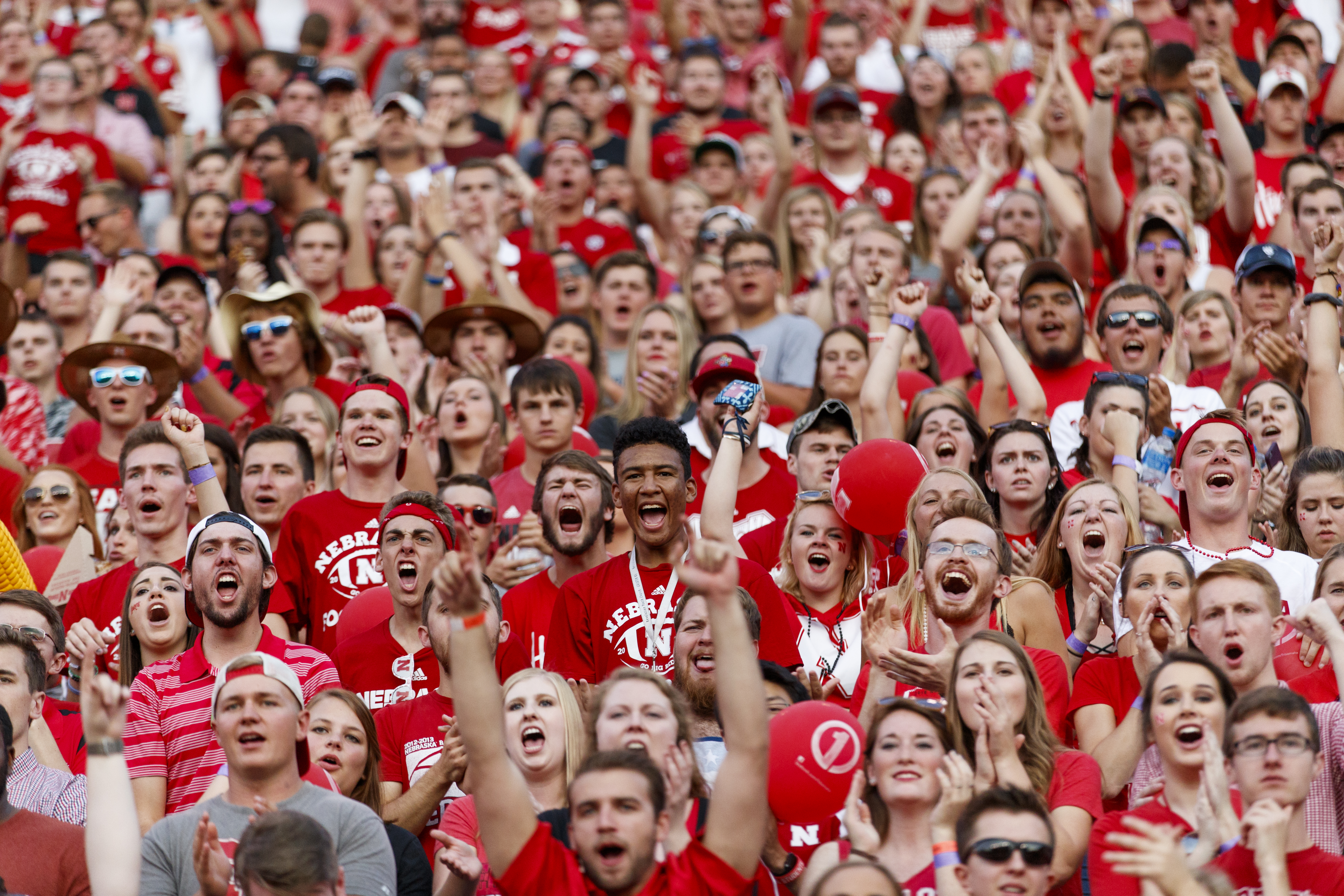 A large crowd of students wearing red cheers at a football game